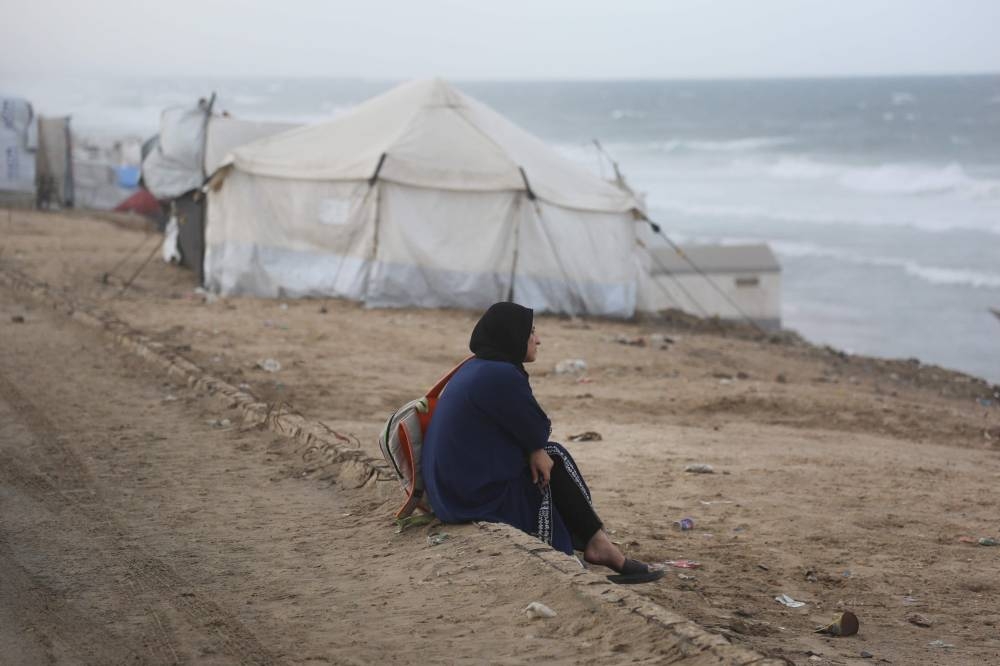A displaced Palestinian woman sits on the beach near tents west of Deir al-Balah city in the central Gaza Strip, on November 15, 2025 as a low-pressure system impacts the area. (AFP)