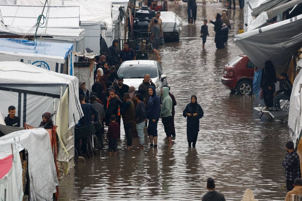 Displaced Palestinians gather next to tents in a flooded area, during a rainy day in Gaza City, November 25, 2025. REUTERS