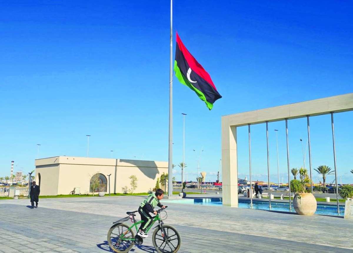 A child cycles past a Libyan national flag flying at half-mast in Tripoli on December 24, 2025, after the head of Libya's armed forces and his four aides died in a plane crash in Turkey. Lieutenant General Mohammed al-Haddad and four other aides were returning to Tripoli on December 23 after holding talks in Ankara with Turkish military officials. The plane carried eight passengers including three crew members. (AFP)