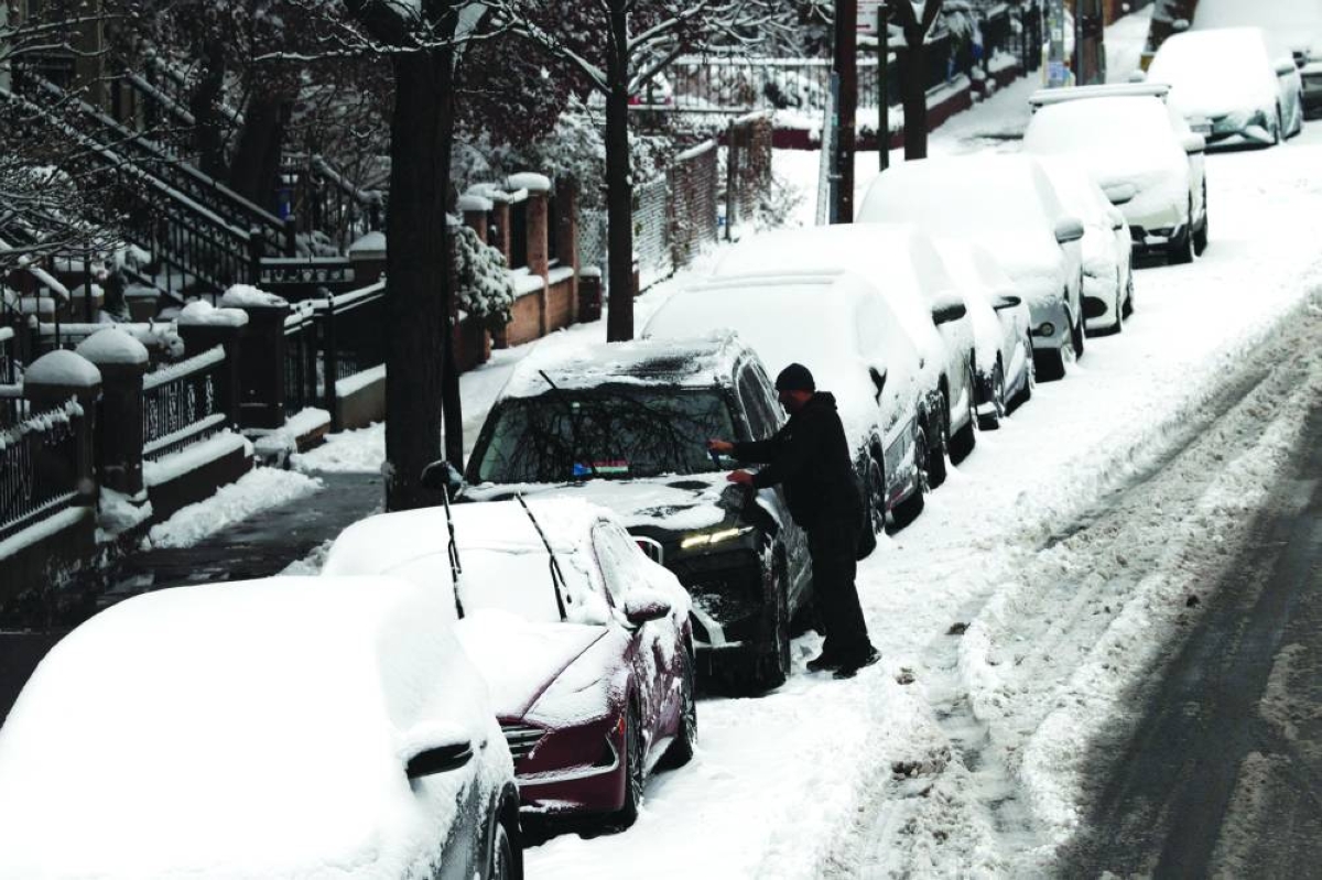A man cleans off his car of snow in Brooklyn after an overnight storm, in New York City, Saturday.