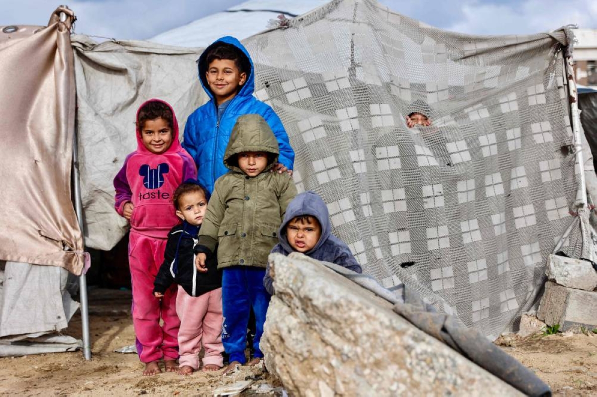Displaced Palestinian children pose for a photograph outside their tent-home as the region experiences rain and cold winter conditions, in Gaza City an December 28, 2025. The majority of Gaza's 2.4 million people have been displaced, often multiple times, by the war that began with Hamas's attack on southern Israel on October 7, 2023. With many displaced living in tent camps, raising serious concerns over winter. (AFP)