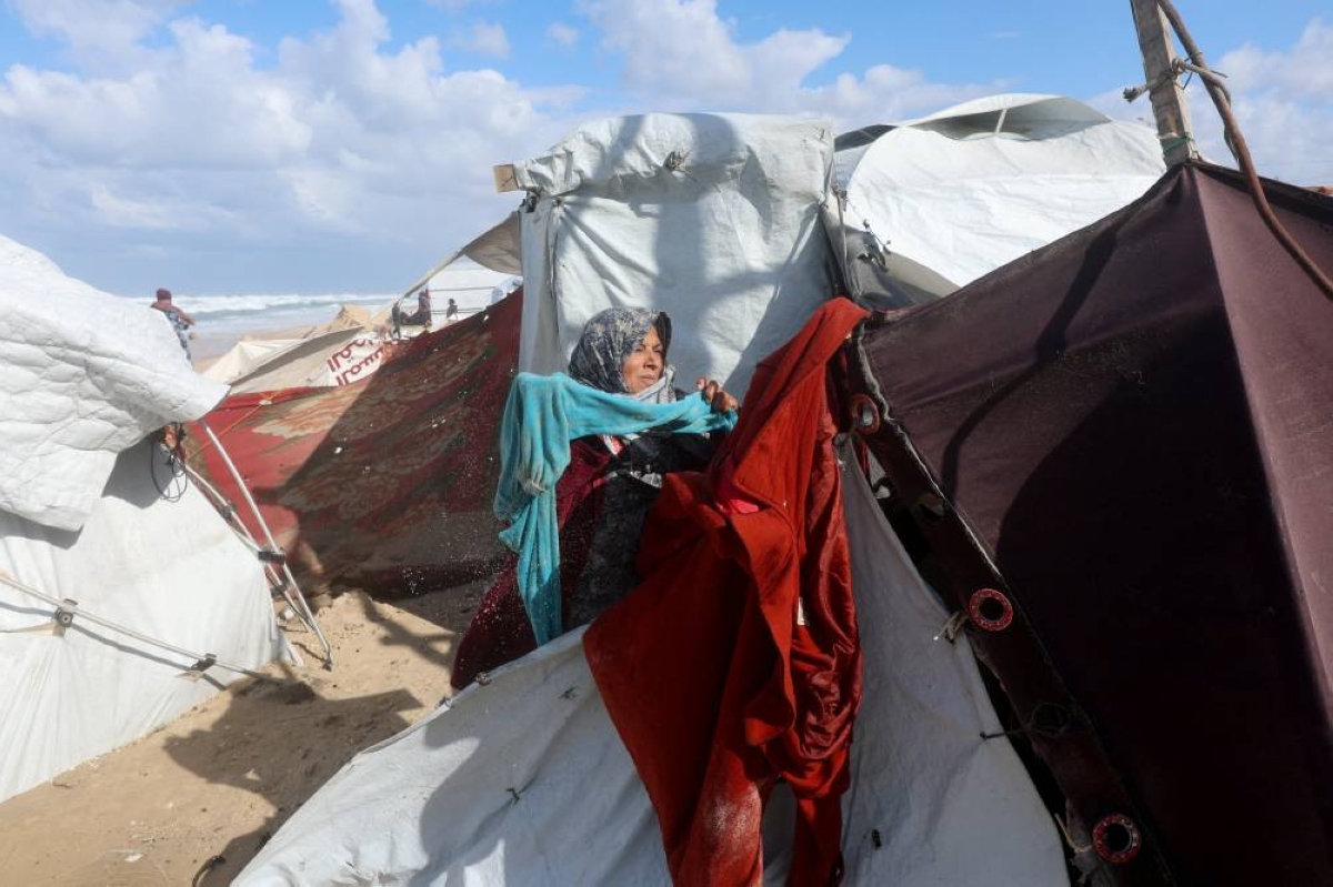 A displaced Palestinian woman collects wet clothes at a beach tent camp, after it was flooded by rising seawater during a winter storm in Khan Younis, southern Gaza Strip, December 28, 2025. REUTERS