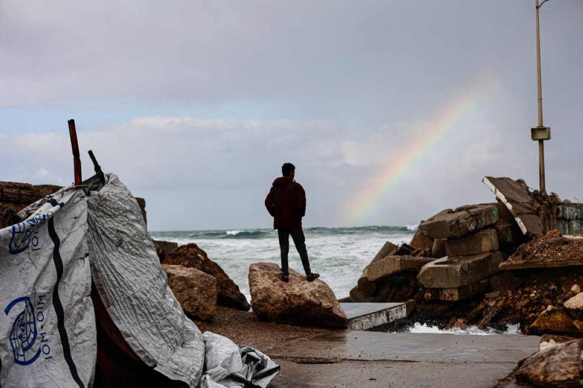 TOPSHOT - A displaced Palestinian man stands outside the family tent shelter erected in the harbour, as he looks at a rainbow out at sea, as the region experiences rain and cold winter conditions, in Gaza City an December 28, 2025. The majority of Gaza's 2.4 million people have been displaced, often multiple times, by the war that began with Hamas's attack on southern Israel on October 7, 2023. With many displaced living in tent camps, raising serious concerns over winter. (AFP)
