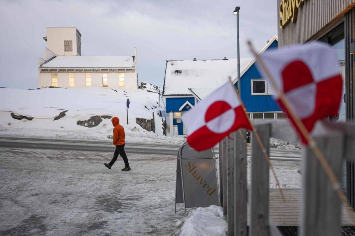 MAIN PICTURE: Greenlandic flags are seen in the foreground as a pedestrian walks along a snowy street in Nuuk, Greenland.