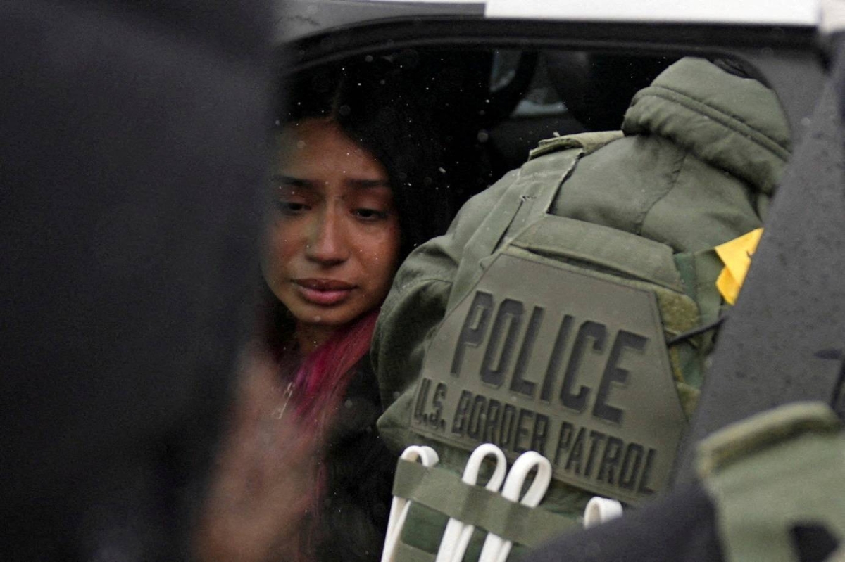 A detained woman sits inside a vehicle surrounded by federal agents, as immigration enforcement continues in Minneapolis. – Reuters