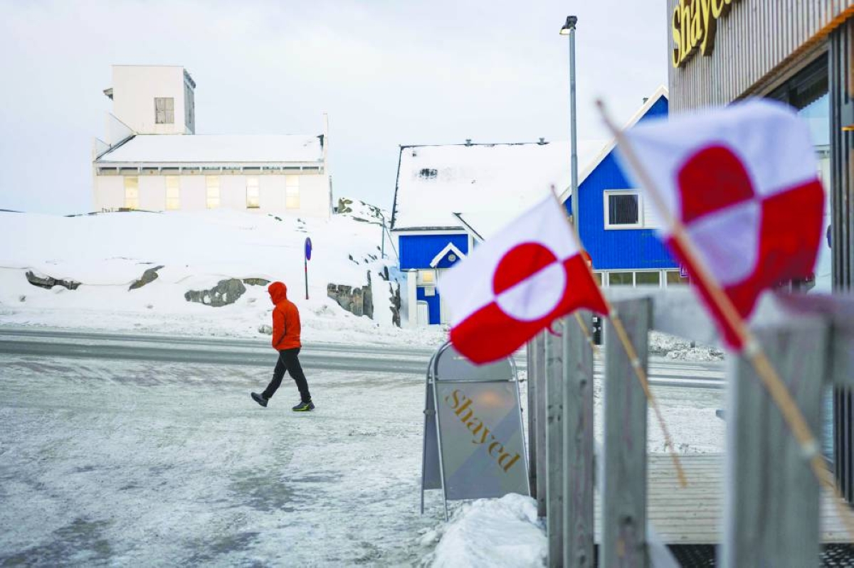 
Greenlandic flags are seen in the foreground as a pedestrian walks along a snowy street in Nuuk, Greenland. 