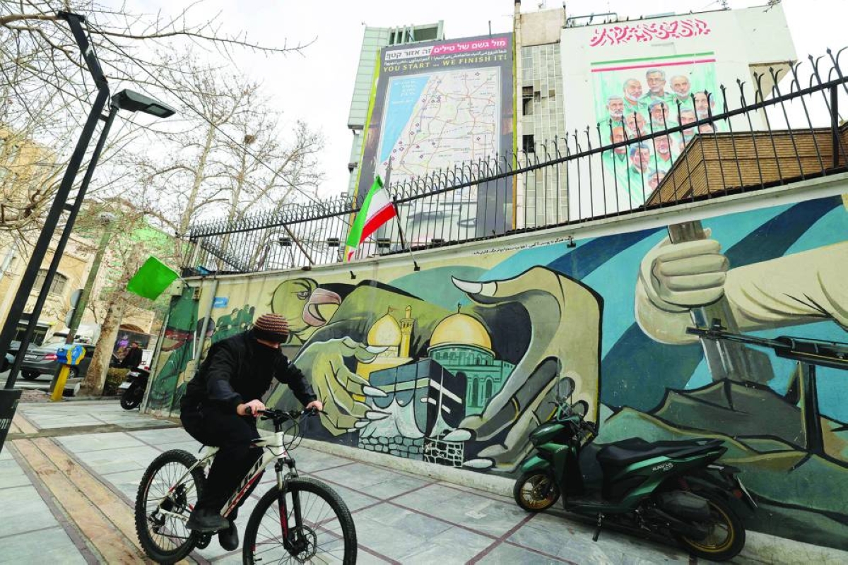 A man cycles past a mural and a giant billboard in Palestine Square, in Tehran, Monday.