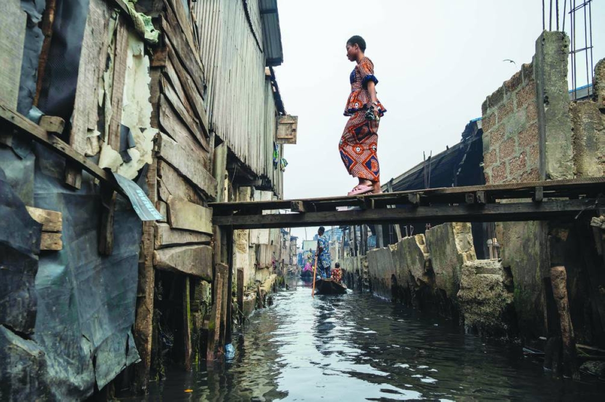 A resident walks on a makeshift bridge as people in pirogues navigate their way in Makoko, a floating slum in Lagos, on January 9, 2026. Authorities have demolished hundreds of wooden shacks in Makoko, Africa’s largest and most iconic floating slum, which is built on stilts above the lagoon in the heart of Lagos. The operation is part of an ongoing campaign to remove what officials describe as illegal structures and reclaim waterfront land for modern real-estate developments. (Photo by TOYIN ADEDOKUN / AFP)