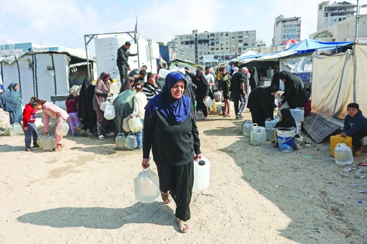 A displaced Palestinian woman carries water containers after filling them from mobile cisterns in the Al-Rimal shelter camp in Gaza City on February 21, 2026. (AFP)