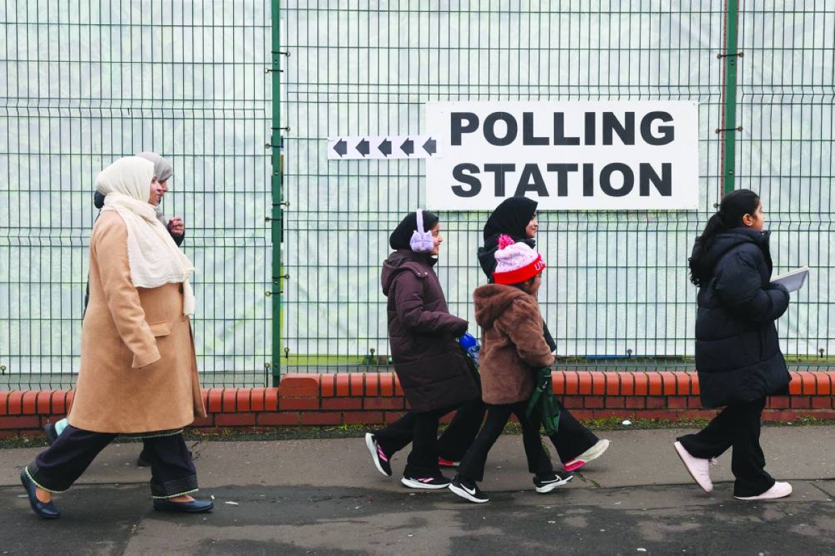 Women and children walk past a signage outside a polling station at St. Agnes Primary School, on the day of the Gorton and Denton by-election, triggered by the resignation of Andrew Gwynne, in Gorton, Manchester, Britain, Thursday.