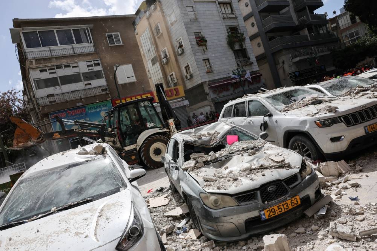 Heavy machinery operates next to damaged cars covered in debris at an impact site, following a barrage of missiles launched from Iran, in central Israel, yesterday. (Reuters)