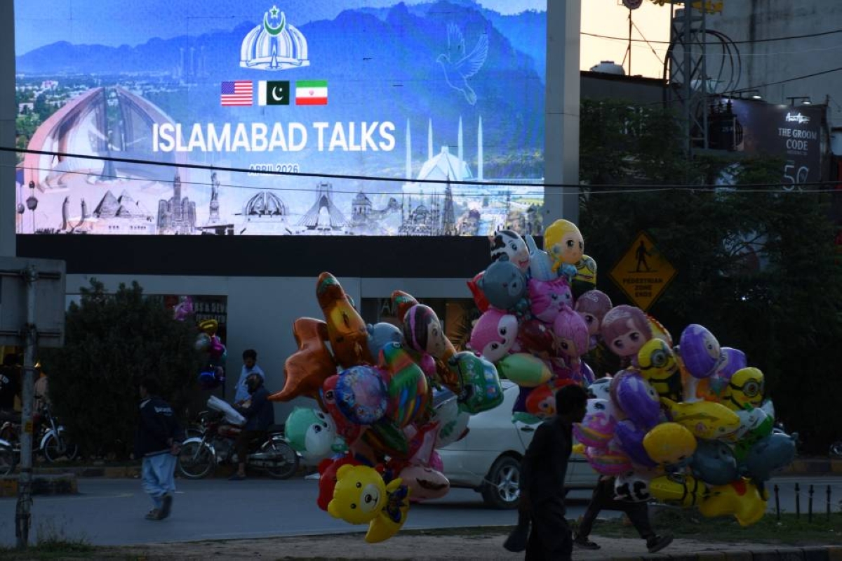 A balloon seller walks near a screen with an image referring to the US-Iran peace talks in Islamabad. (Reuters)