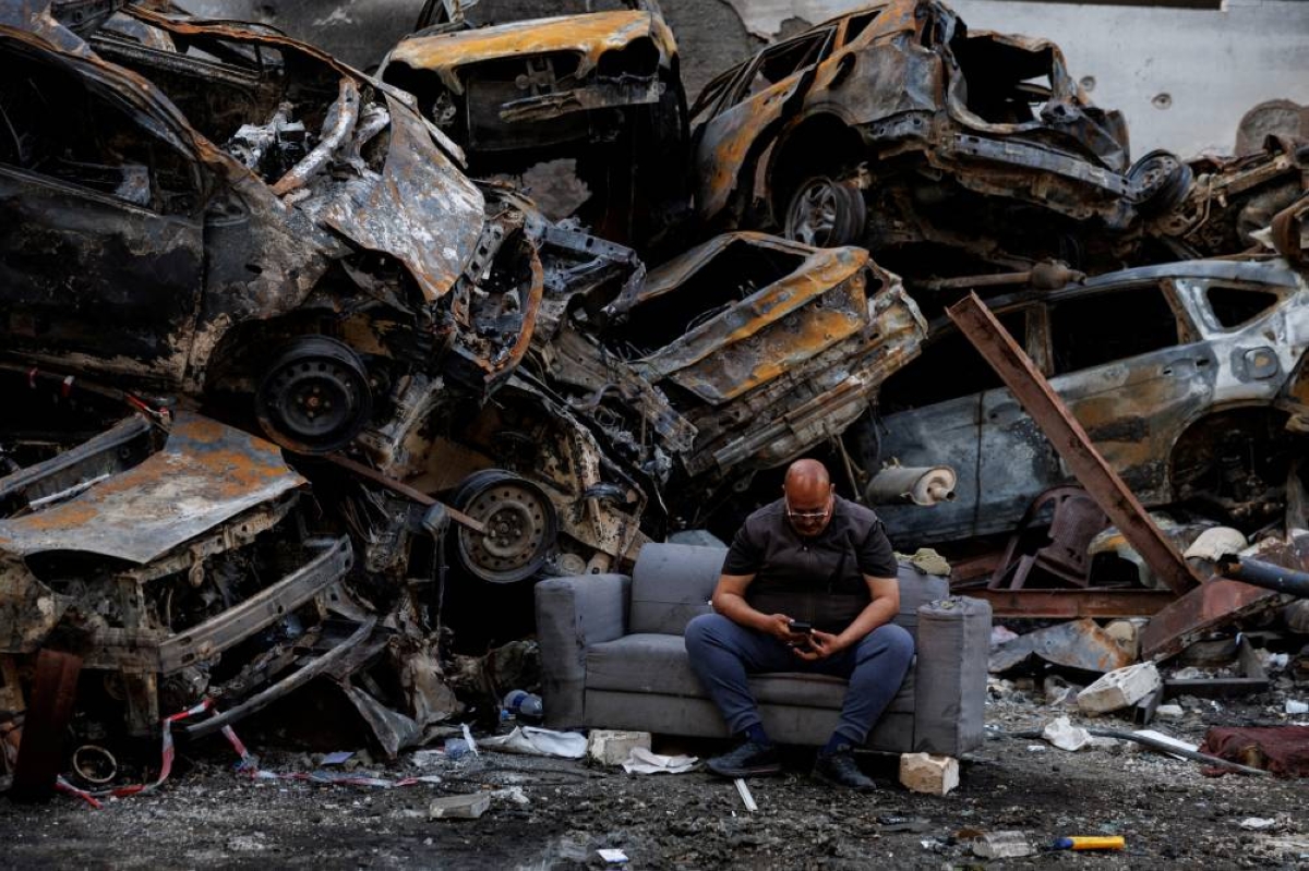 Mohamed El Junayd, 43, who said he survived the Israeli strike, sits beside piled damaged cars at the site of an Israeli strike carried out on April 8, at Corniche al-Mazraa in Beirut, Lebanon, yesterday. (Reuters)