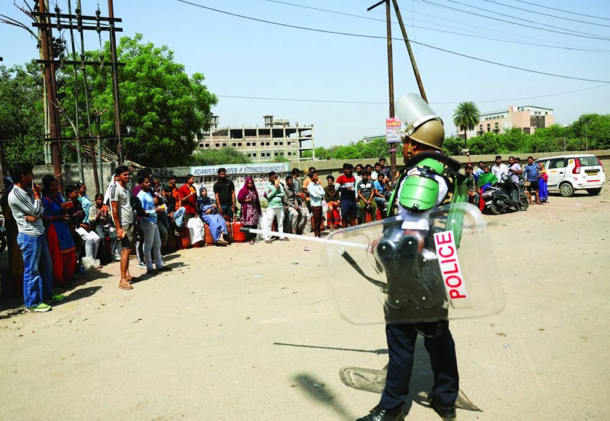 A police officer stands as people queue to get LPG cylinders, after Tuesday's violent protests by factory workers demanding wage hikes amid rising living costs linked to the US-Israeli conflict with Iran, in Noida, Tuesday. (Reuters)