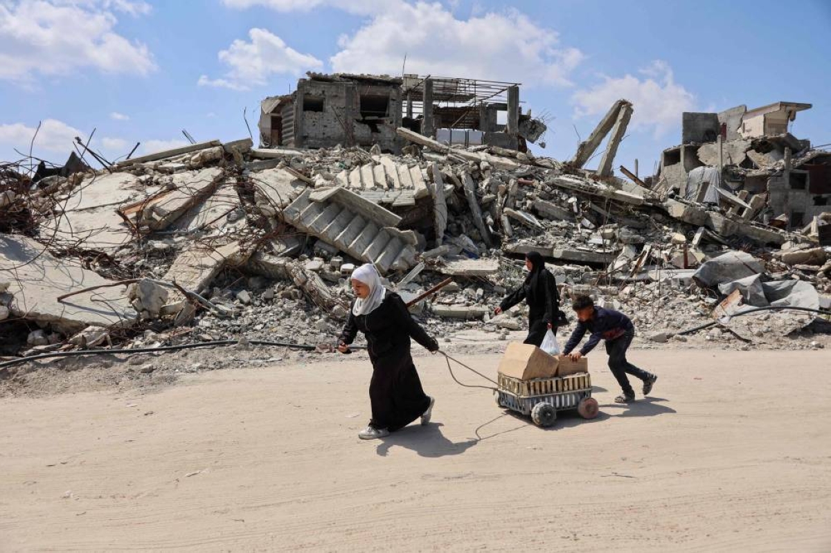 TOPSHOT - Displaced Palestinians carry boxes in a cart past the rubble of destroyed buildings at the Jabalia refugee camp in the northern Gaza Strip on April 13, 2026. Since the terms of a US-brokered ceasefire deal came into effect on October 10, Israel remains in control of nearly half of the Gaza Strip, including all its border areas. Nearly two million people in Gaza are living in makeshift shelters, and the humanitarian situation remains dire, according to aid agencies. (Photo by Omar AL-QATTAA / AFP)