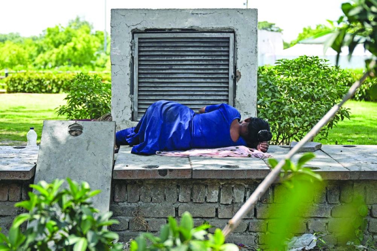 A woman sleeps next to an air conditioner vent exuding cool air at a park on a hot summer afternoon in New Delhi Wednesday. (AFP)