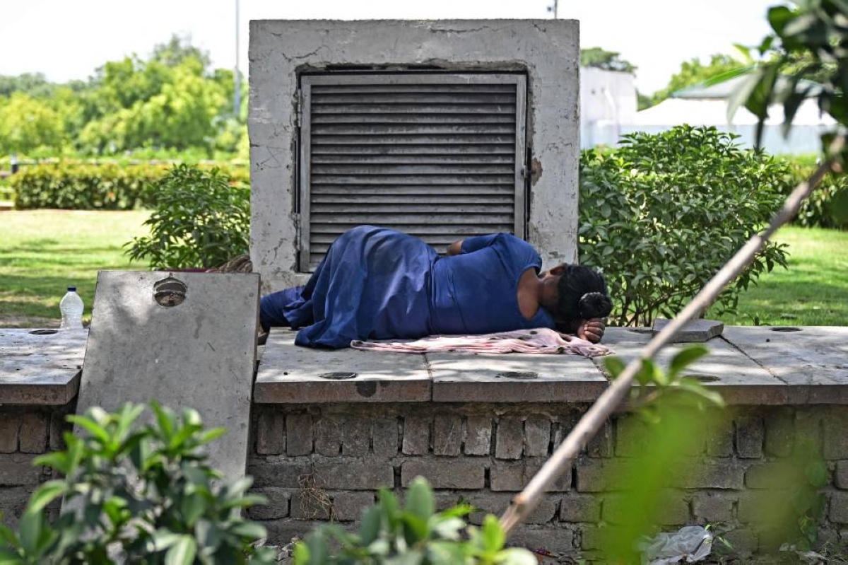 A woman sleeps next to an air conditioner vent exuding cool air at a park on a hot summer afternoon in New Delhi yesterday. (AFP)