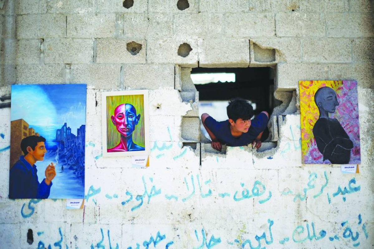 A child looks through damaged wall at an open-air art exhibition at the Bureij camp for Palestinian refugees in the Gaza Strip Tuesday. (AFP)