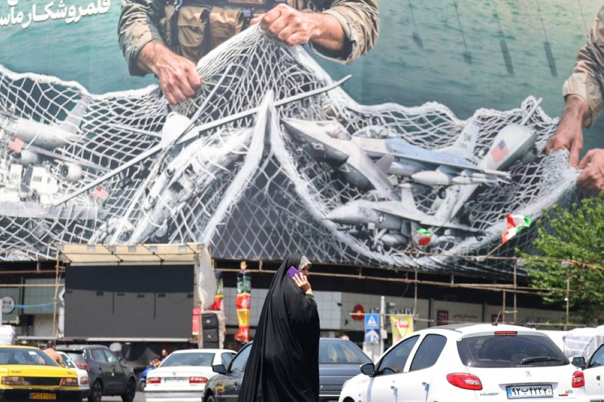 A woman walks past a giant billboard reading "The Strait of Hormuz remains closed" at the Revolution Square in Tehran. (AFP)