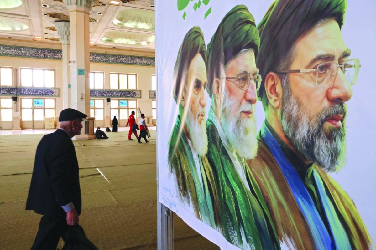 
An Iranian man walks past an image of former and the current Iranian supreme leaders, Ayatollah Ruhollah Khomeini (L), Ali Khamenei, and his son, the current leader Mojtaba Khamenei (R), in Tehran yesterday. (AFP) 