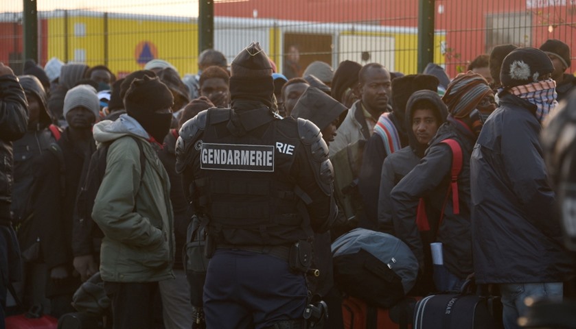 French gendarms stand guard as migrants walk with their bags during the full evacuation