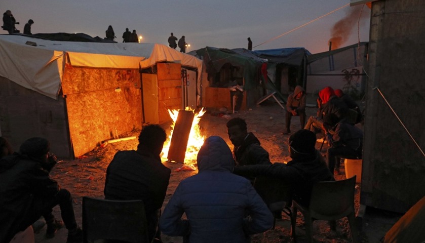 Migrants sit near a fire for warmth at the end of the first day of the evacuation
