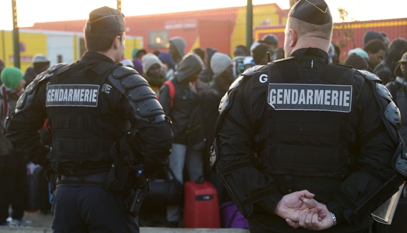 Gendarms stand guard as migrants queue during the full evacuation of the camp