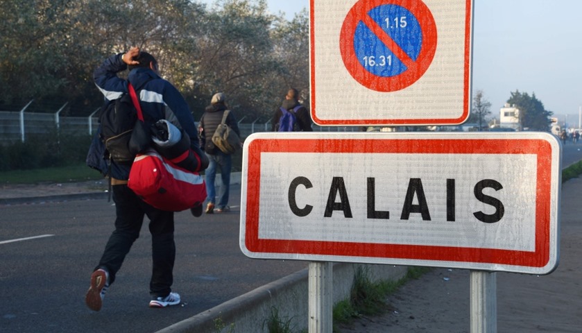 Migrants, carrying their luggage, walk past a Calais city limit sign