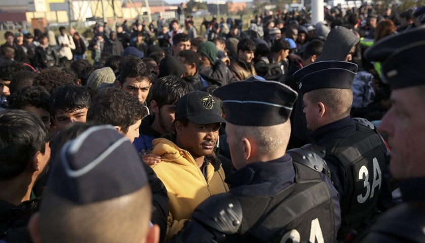 French police stand near as migrants wait in front of a processing centre