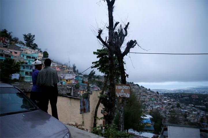 A couple enjoy the view while hurricane approaches Port-au-Prince. The text reads, \'House for Sale\'