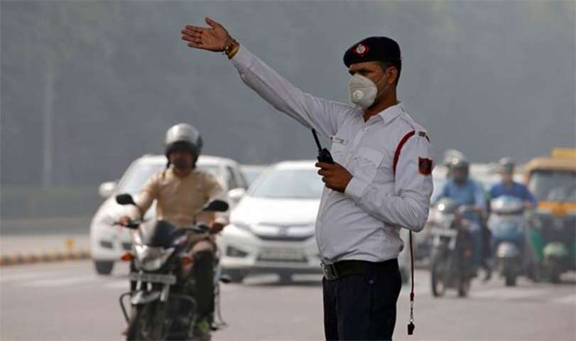 A traffic policeman wearing a mask controls traffic at a busy road in New Delhi