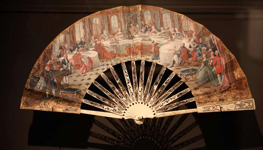 A fan with an illustration representing a royal lunch is seen on display