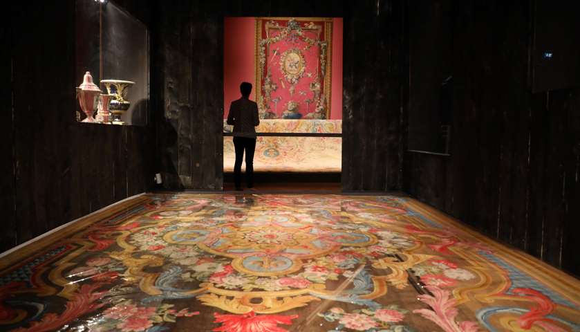 A visitor looks at carpets and furniture on display as part of the \"visiteurs de Versailles\" exhibit
