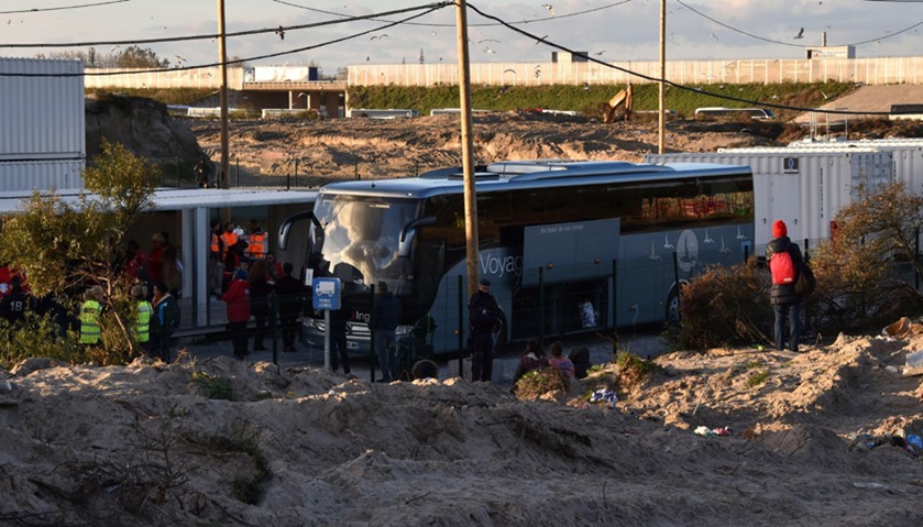 Police officers stand near a bus that will carry unaccompanied migrant minors