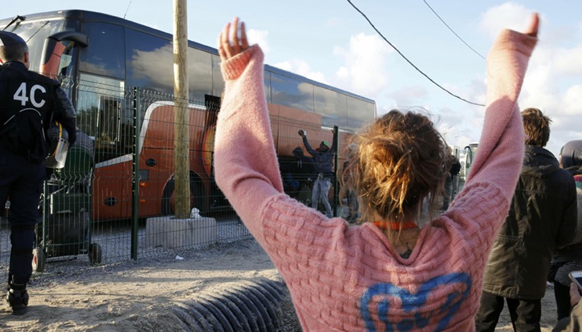 A volunteer waves to migrant minors in a bus during their transfer