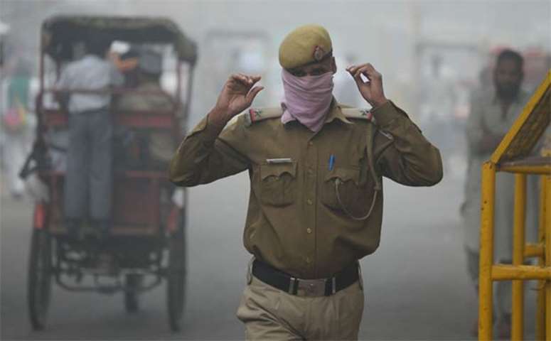 A policeman covers his face with handkerchief as he walks during smog in the Indian capital