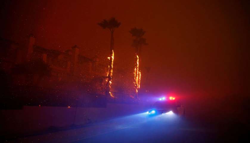 A law enforcement vehicle drives through a neighborhood as the Woolsey Fire burns in Malibu