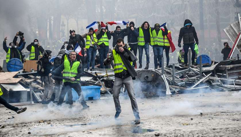Yellow vests protestors shout slogans from a barricade as they clash with riot police in Paris