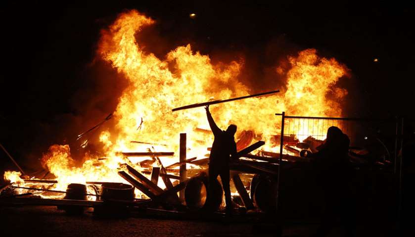 A yellow vest (Gilet jaune) protestor throws material onto a fire on the Champs-Elysees in Paris