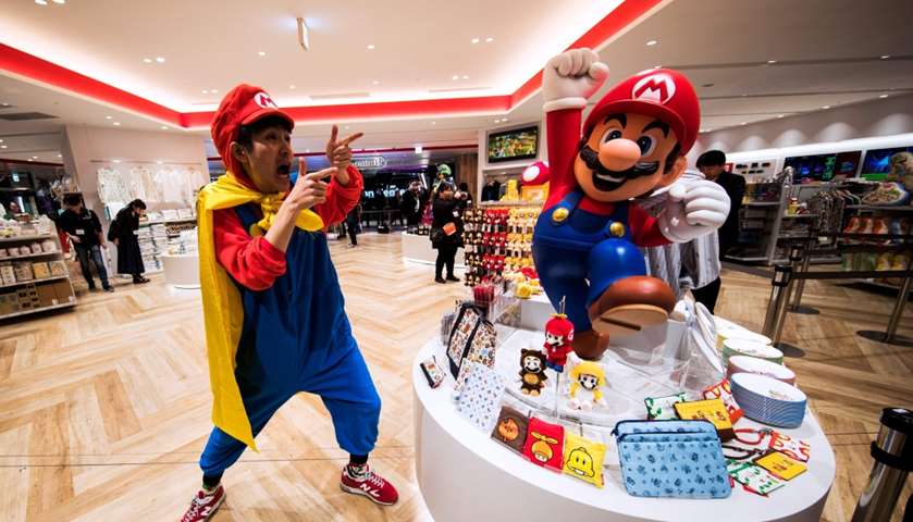 A man wearing a costume of Nintendo game character Mario poses next to merchandise 
