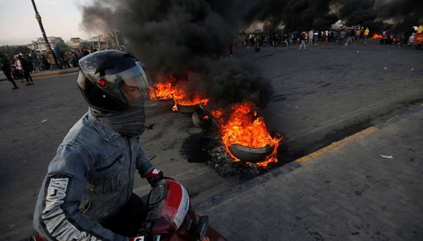 A man rides his motorbike near burning tires during ongoing anti-government protests in Basra, Iraq