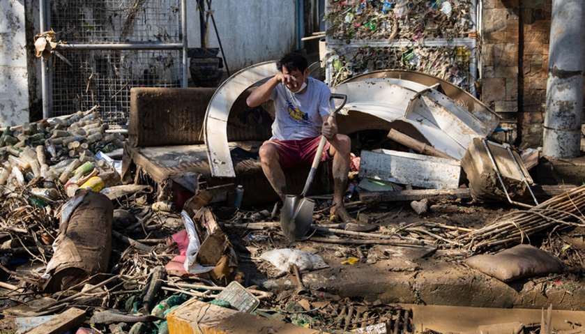 A man reacts as he takes a break from cleaning mud outside his house, which was submerged due to flo