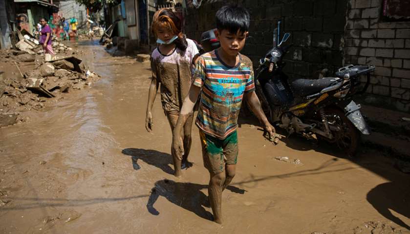 Children wade through muddy floodwater in their community, after flooding caused by Typhoon Vamco