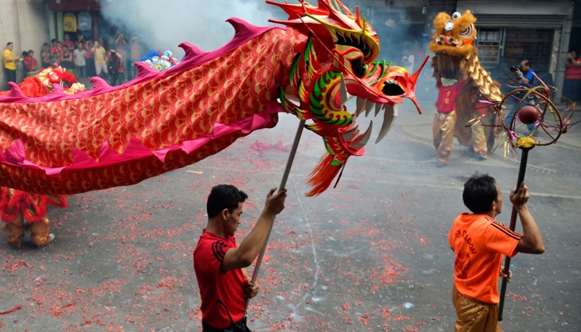 Revellers perform a dragon dance amidst haze caused by firecrackers
