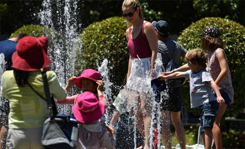 Children and adults play in a fountain on a hot day at the Australian Open on Friday