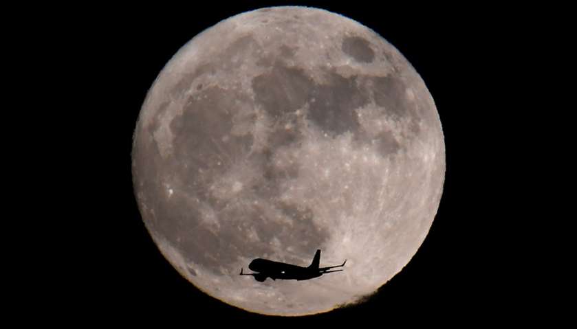 A passenger plane, with a \'supermoon\' full moon seen behind, in London