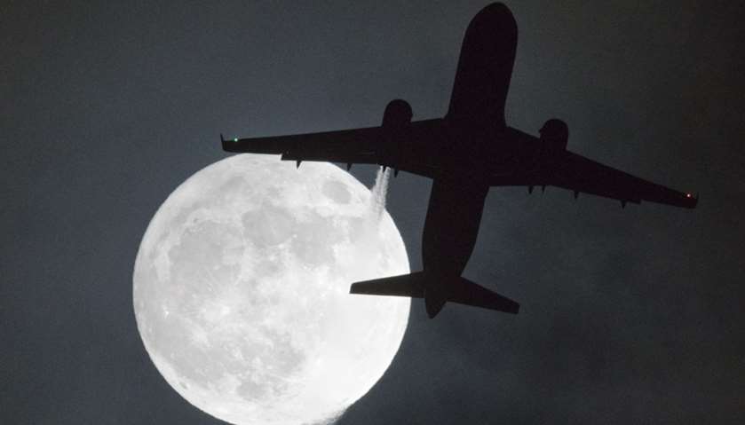 A plane flys in front of a \"super moon\" on its approach to London Heathrow Airport