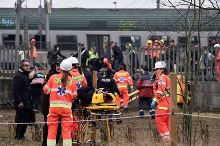 Rescue workers and police officers stand near derailed trains in Pioltello