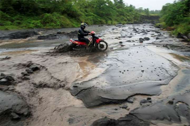 A motorcycle driver crosses a river with lahar from Mount Mayon volcano in Daraga