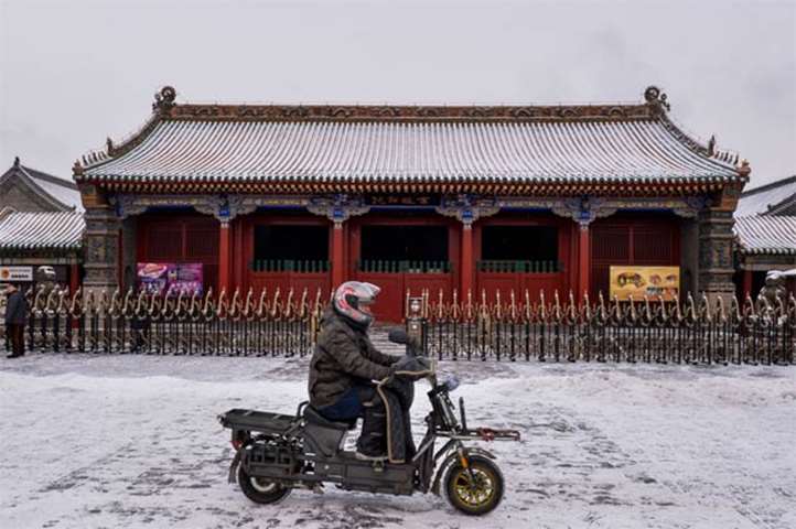 A man rides an electric bike across the snow-covered ground at Shenyang\'s Imperial Palace